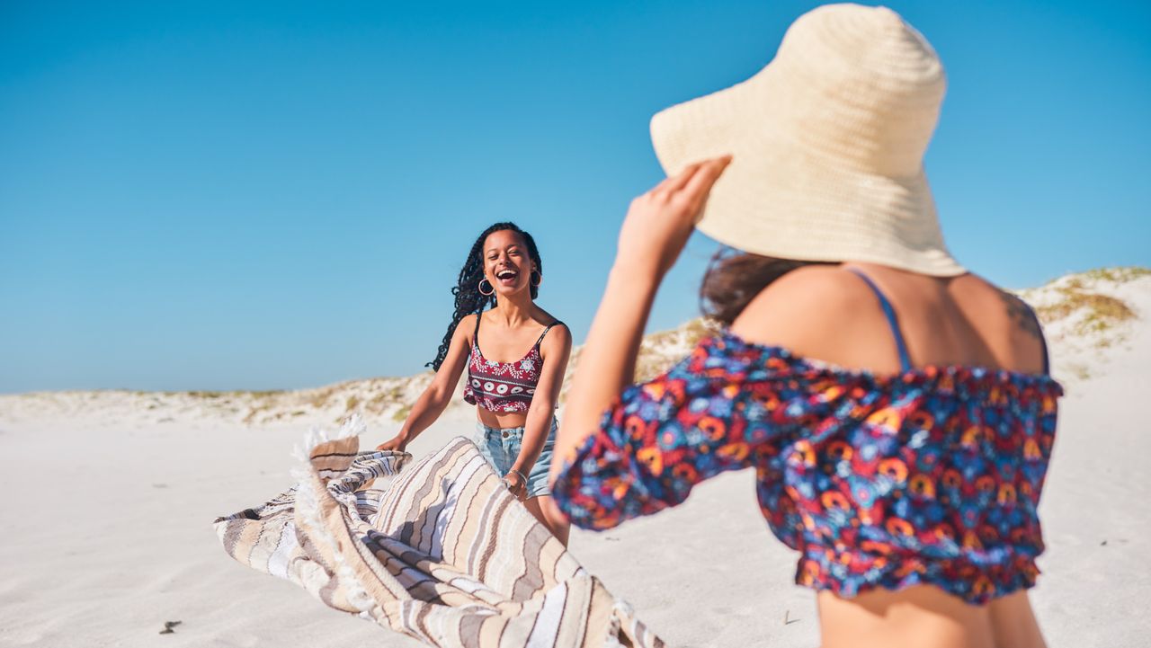 women with towel at the beach trying to lay it flat in the sand