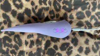 A photograph of the LELO Dot plugged into the charging cable, sitting on a leopard print pillow case
