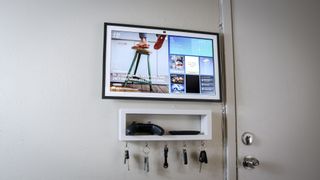 The Echo Show 21 mounted to a wall in the kitchen with a shelf underneath it