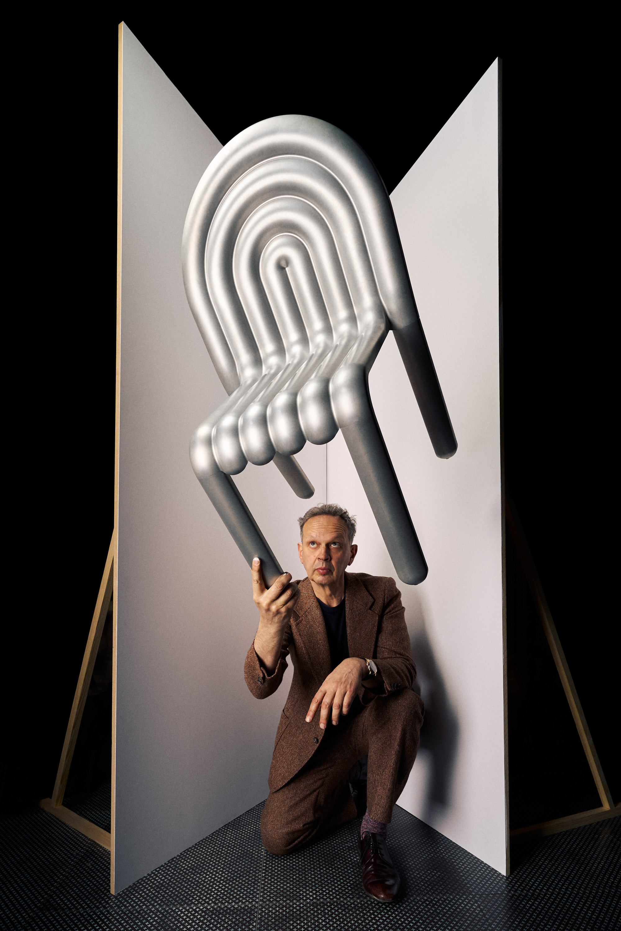 Tom Dixon Recycled aluminium chair held up by man in brown suit