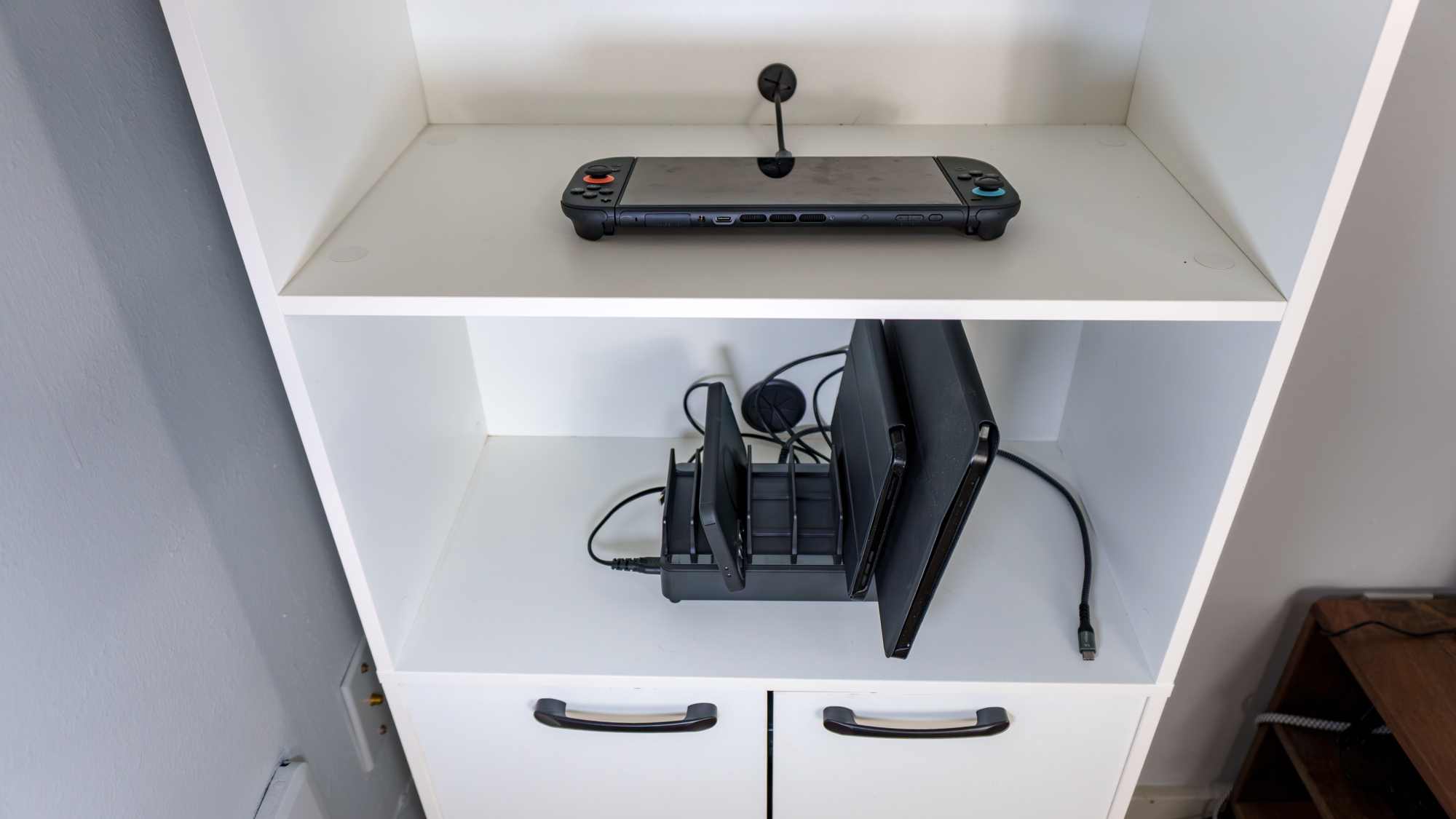 A multi-device charging station and Nintendo Switch 2 connected to a USB-C to Ethernet adapter on the open shelves of a kitchen pantry cabinet