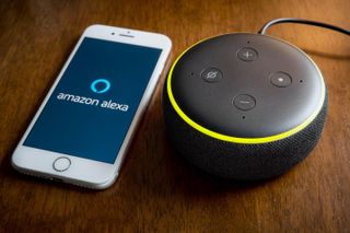 A close up of an Amazon Echo smart speaker and an iPhone with the Alexa app logo