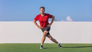 Man outdoors on grass performing a single leg squat variation with hands on hips and right leg extended behind left