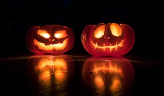 Två halloweenlyktor står bredvid varandra i mörkret.