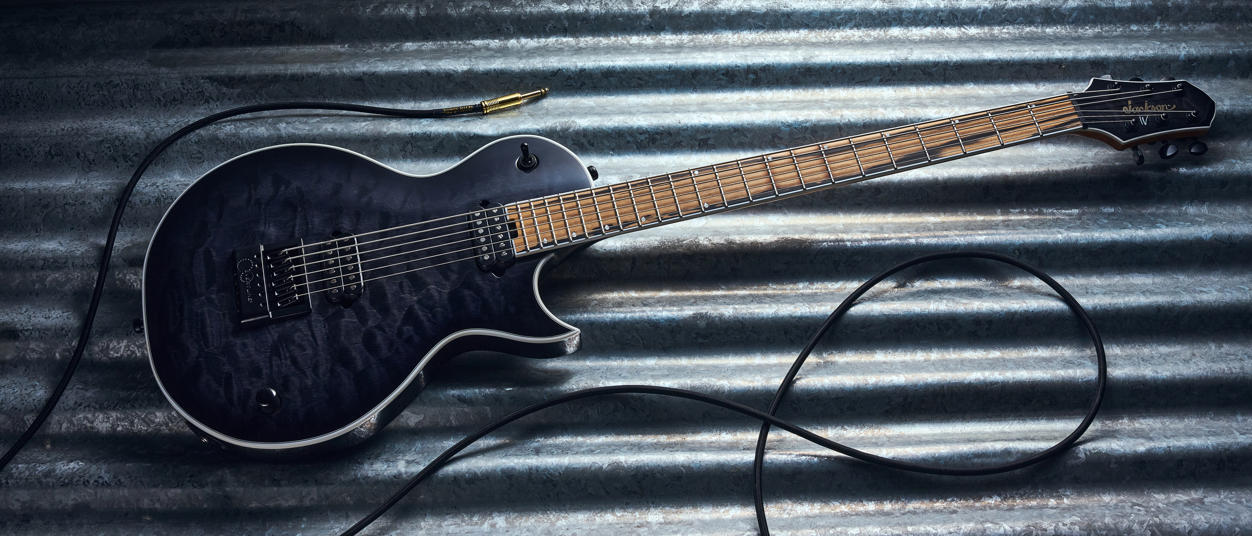 The Jackson Signature Sleep Token IV Monarkh electric guitar lying on a piece of sheet metal with a guitar cable coiled nearby
