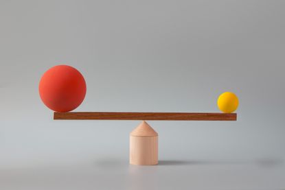 a large red sphere and a small yellow one balancing on piece of wood