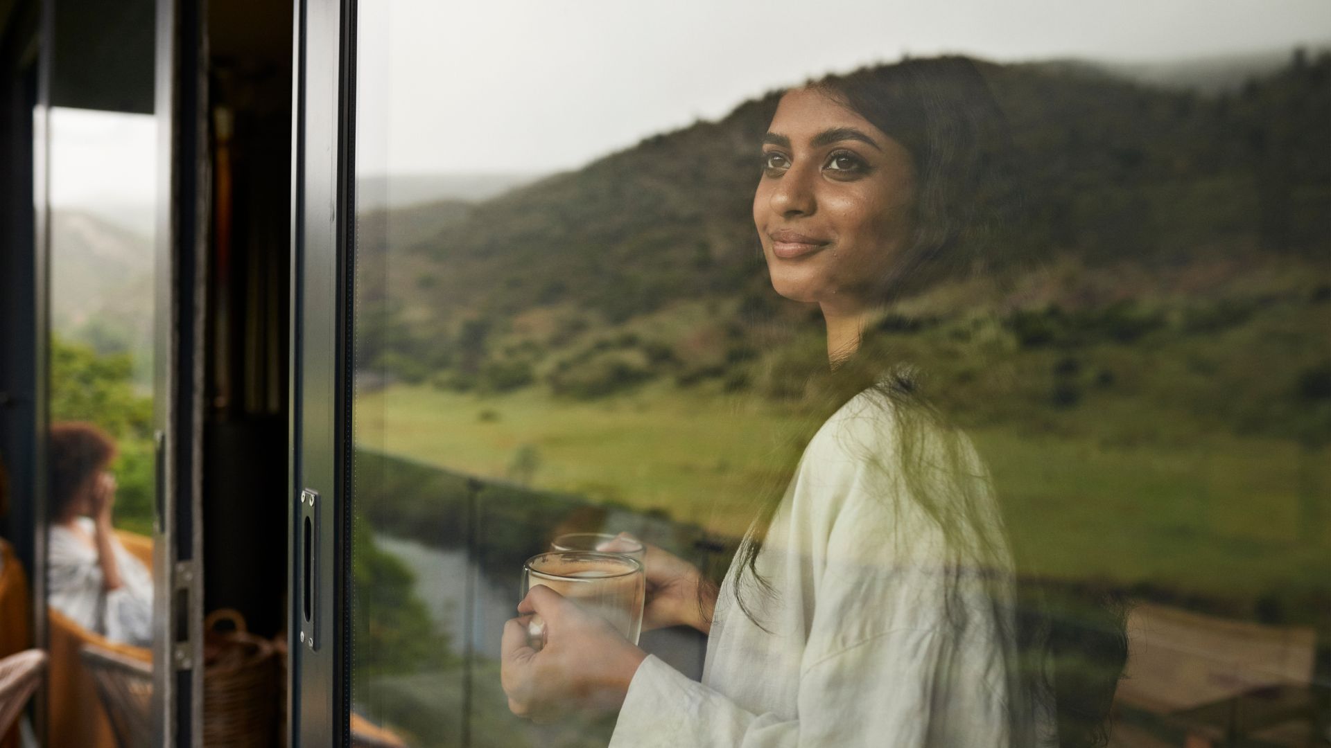 Woman looking out of the window into morning sunlight holding mug