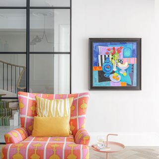 Pink armchair with yellow cushions, pink side table, hanging artwork with glass wall partition