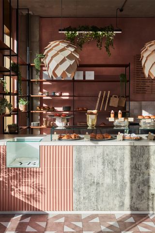 A rose-hued, vintage-inspired bakery features aesthetically pleasing interiors including a mosaic floor, pendant sculptural lamps, and trailing plants.