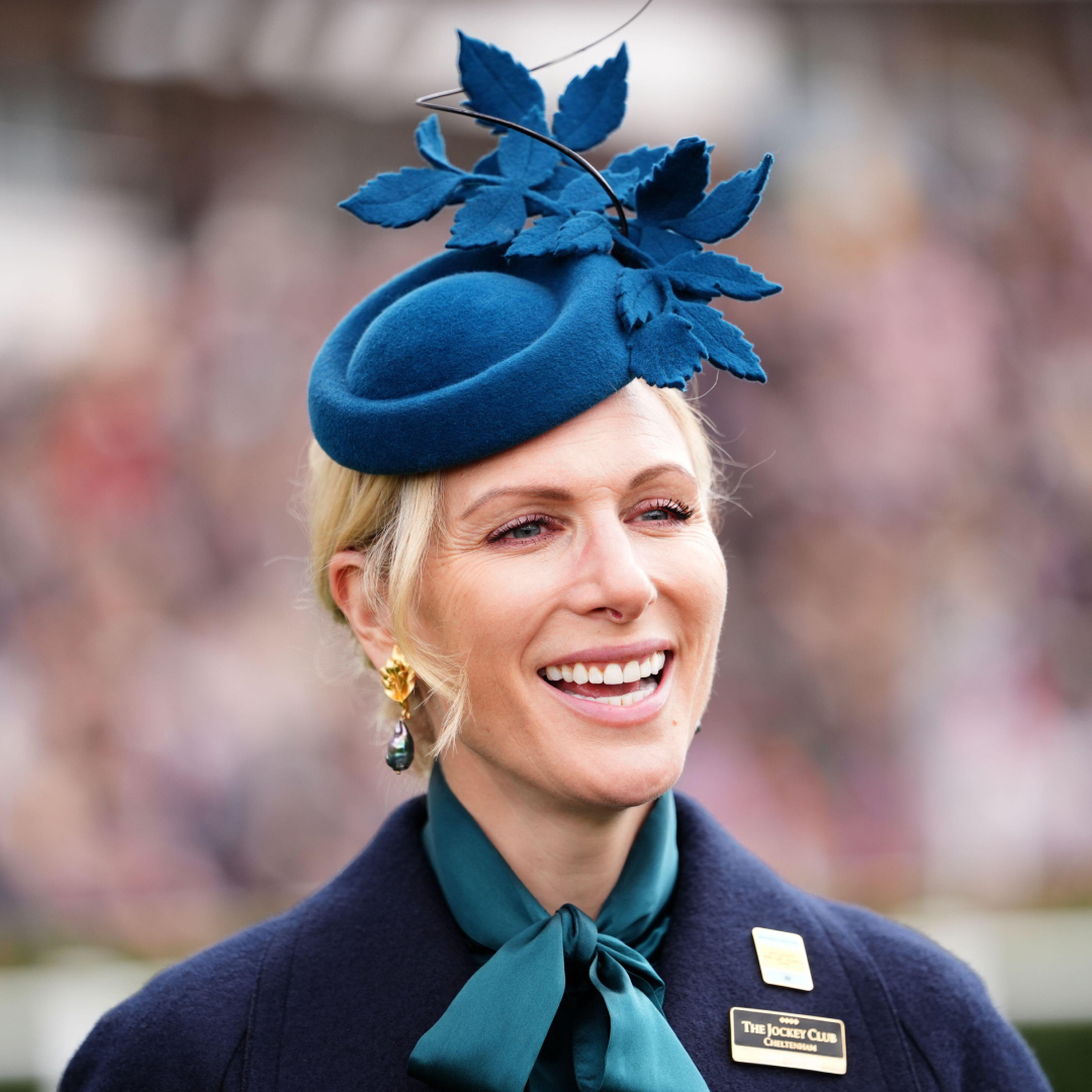 Zara Tindall smiling in a blue hat and tie neck blouse