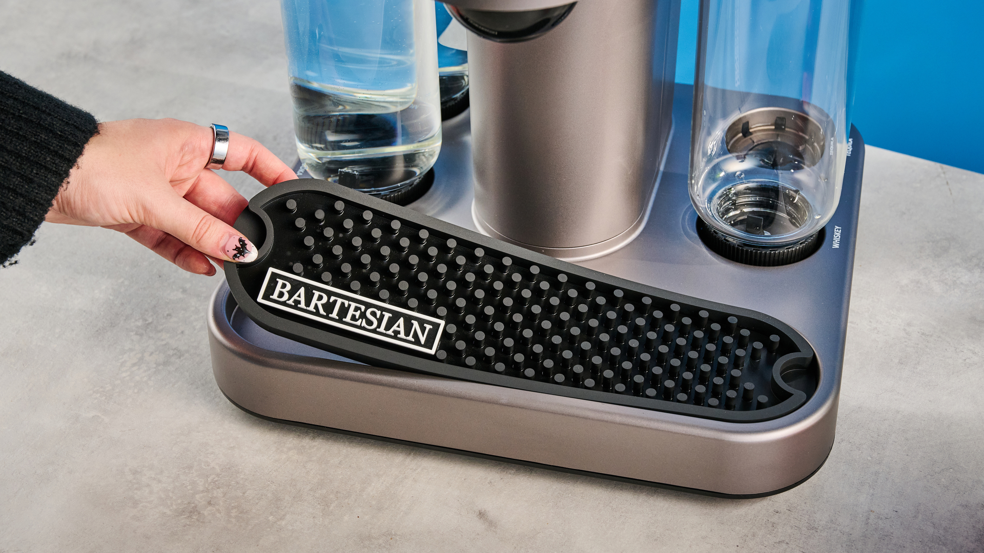 the bartesian premium cocktail machine photographed against a blue background showing its drink-making abilities and accessories and functionality with cocktail pods
