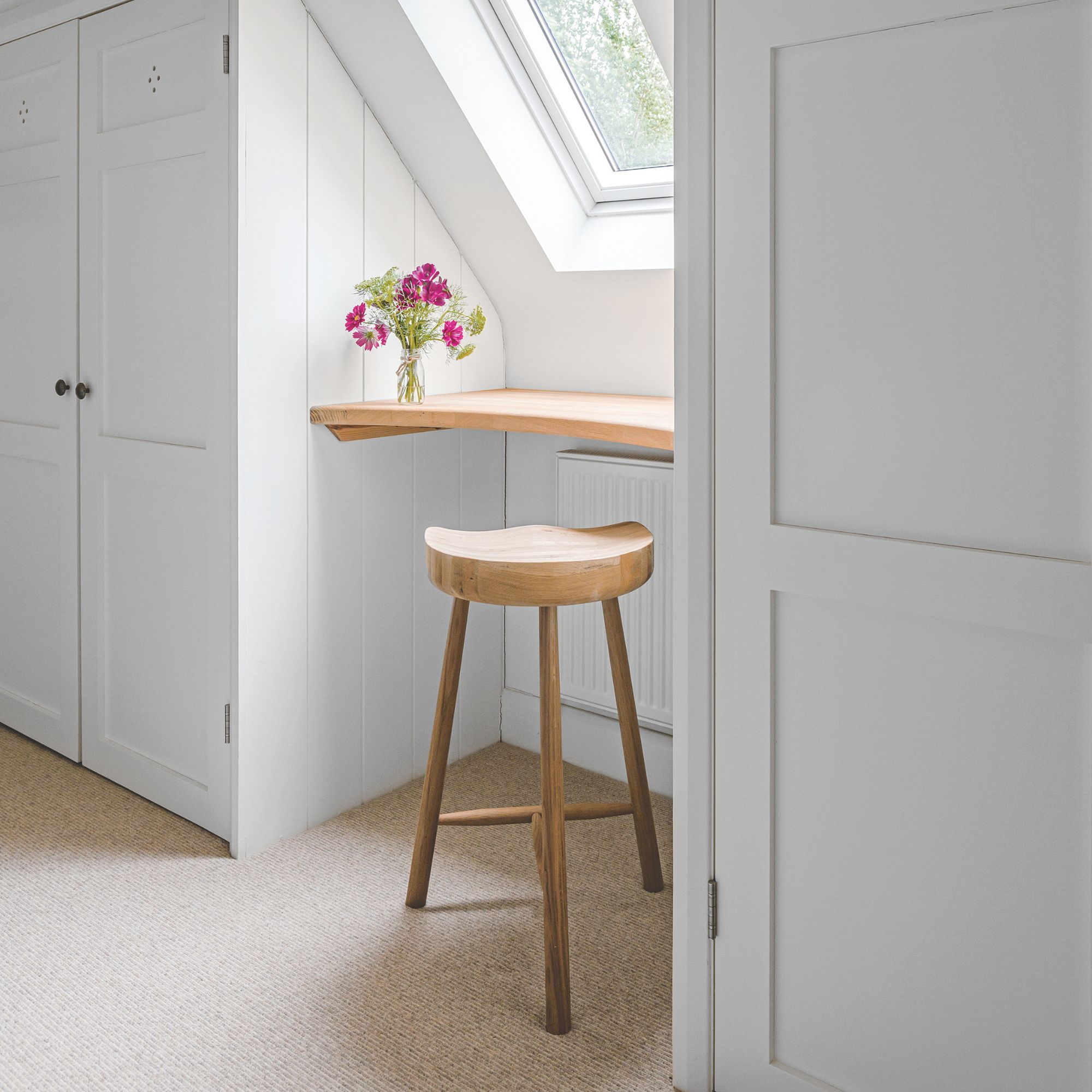 Carpeted dressing area in a bedroom recessed into a velux window space, with a wooden shelf and stool