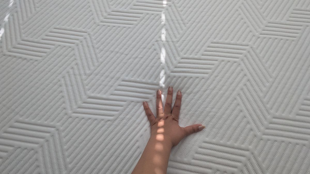A hand placed on the Emma Hybrid Airgrid mattress checking the firmness