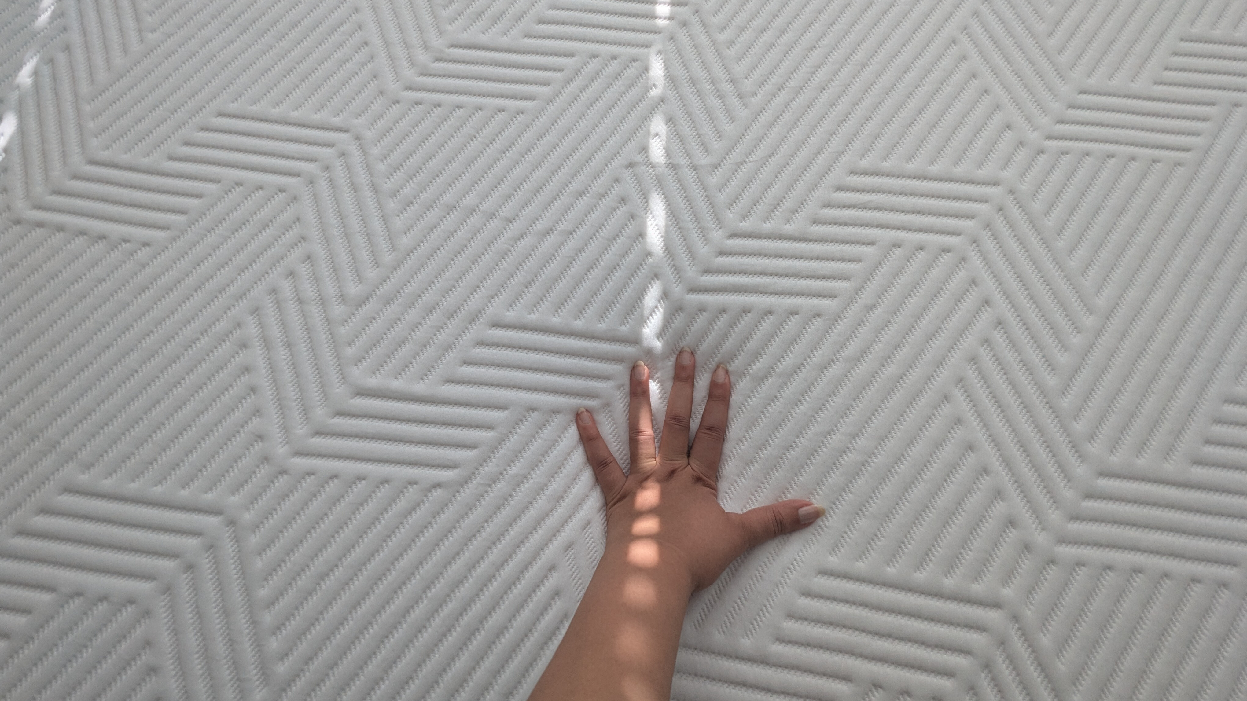 A hand placed on the Emma Hybrid Airgrid mattress checking the firmness