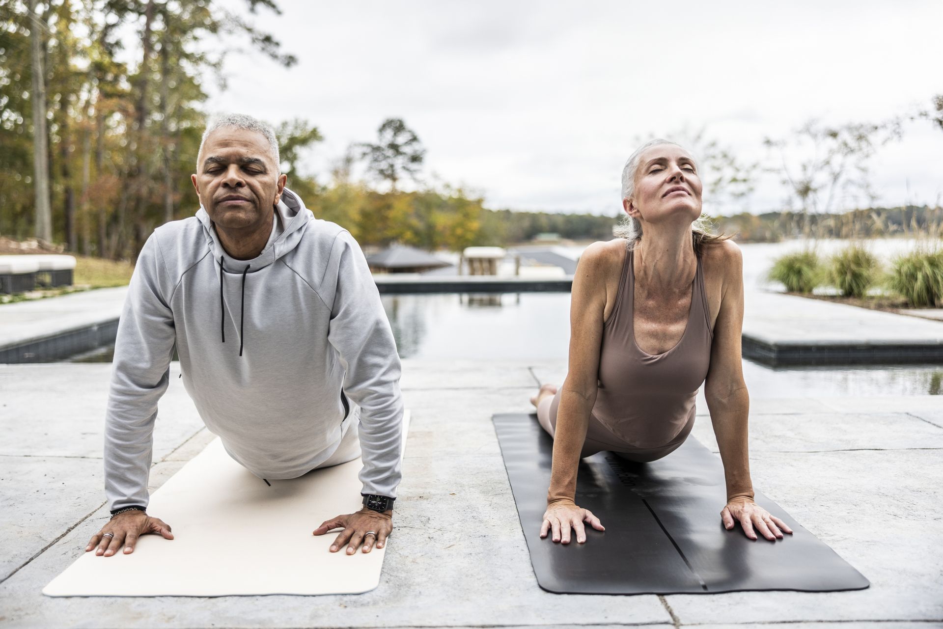 Senior couple doing yoga in front of beautiful pool overlooking lake