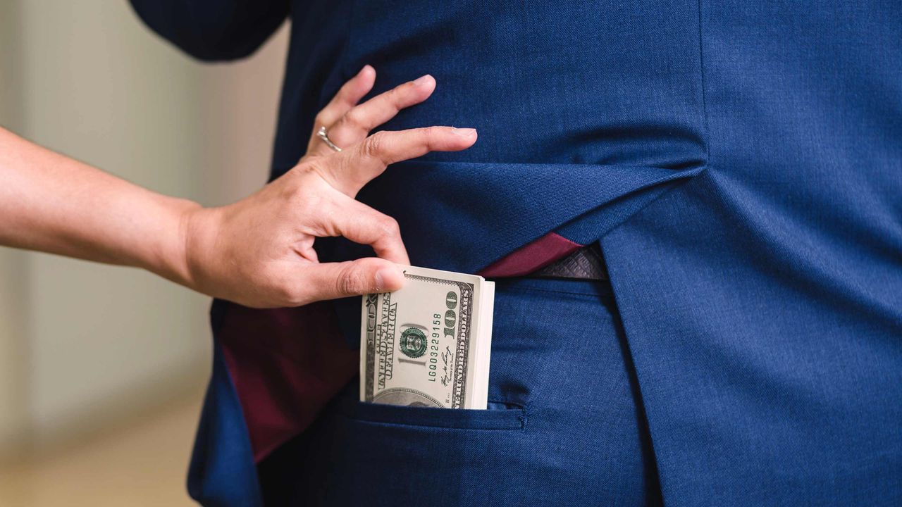 A hand snatches cash out of the back pocket of a man&amp;#039;s suit pants.