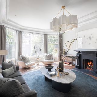 A white living room with a fireplace, grey sofa and chairs and a coffee table in a house which once belonged to Meg Ryan