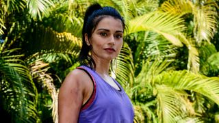 Chaz (Bhavna Limbachia) stands in the forest, wearing a purple workout vest