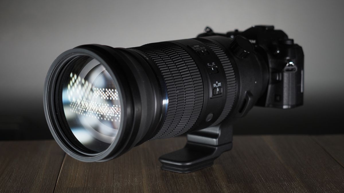 OM System M.Zuiko 150-600mm f/5.0-6.3 IS lens, mounted to an OM System OM-1 Mark II, on a wooden surface lit with moody lighting