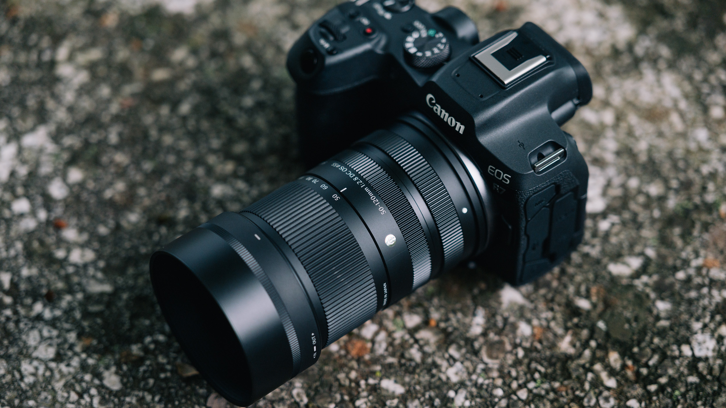 Sigma 50-120mm F2.8 DC OS Contemporary lens attached to a Canon EOS R7, rested on a rock