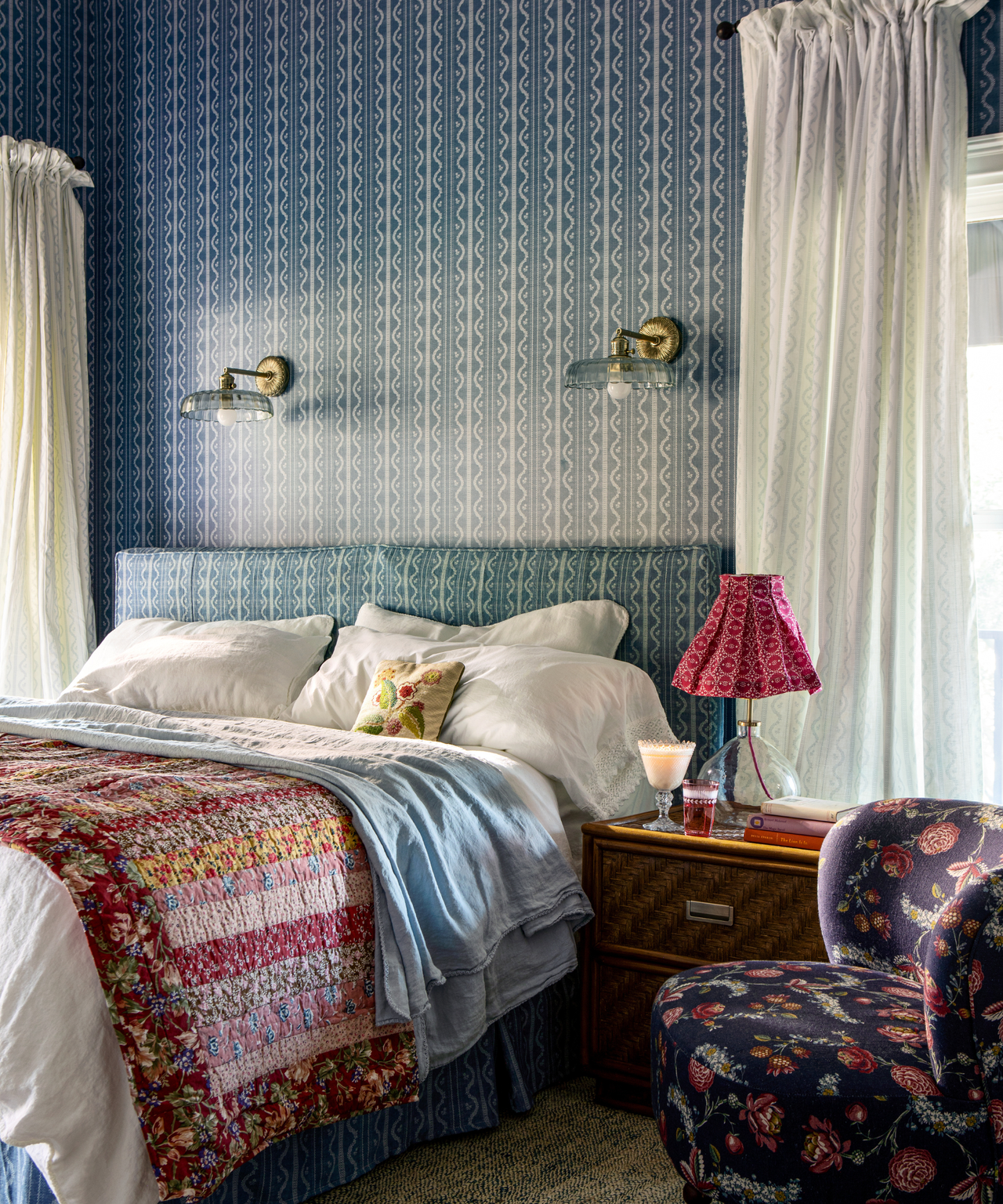 a cozy bedroom with blue wallpapered walls, a layered bed, and a dark blue floral accent chair