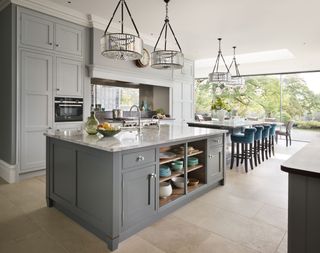 A large gray painted kitchen with pendant lighting over the kitchen island and dining table.