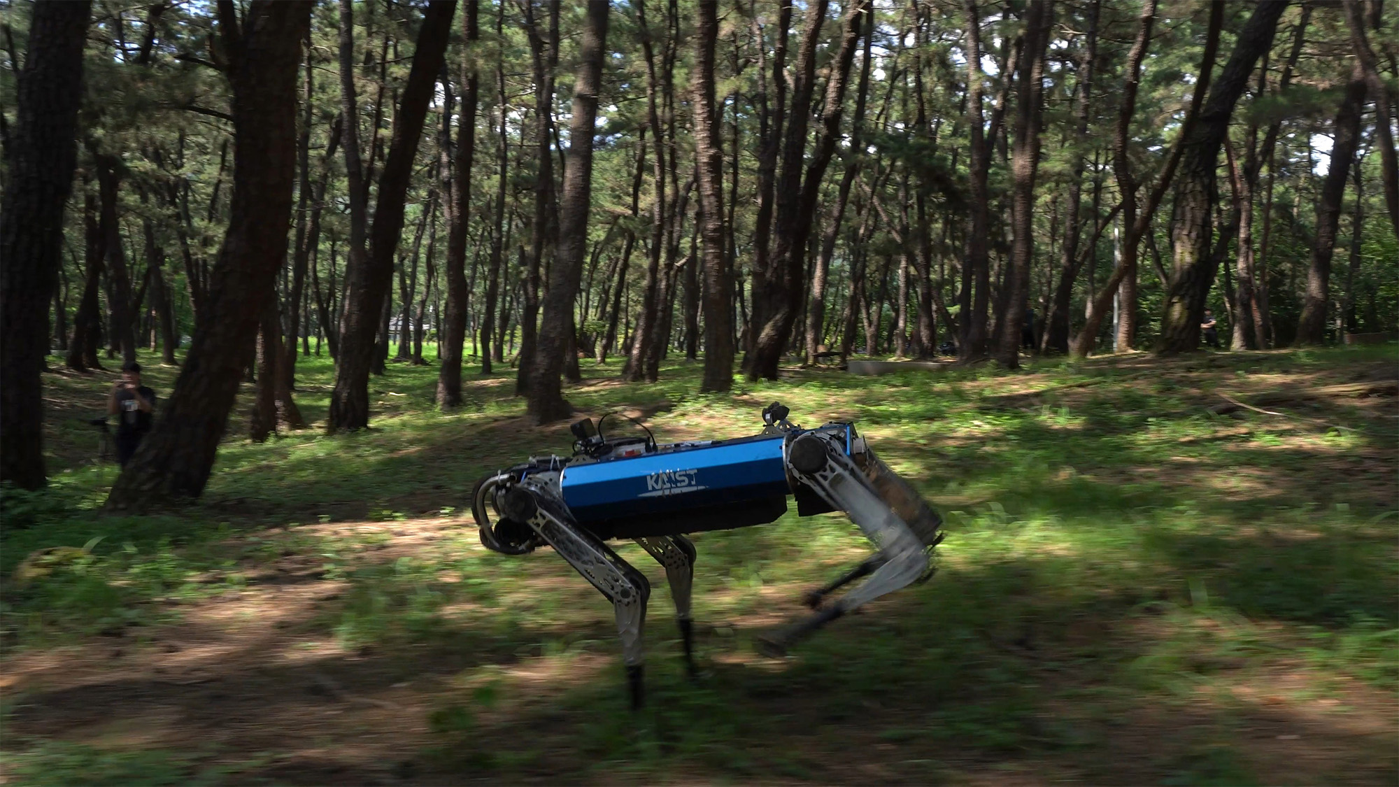A four-legged robot dog with a blue torso runs through a forested landscape.