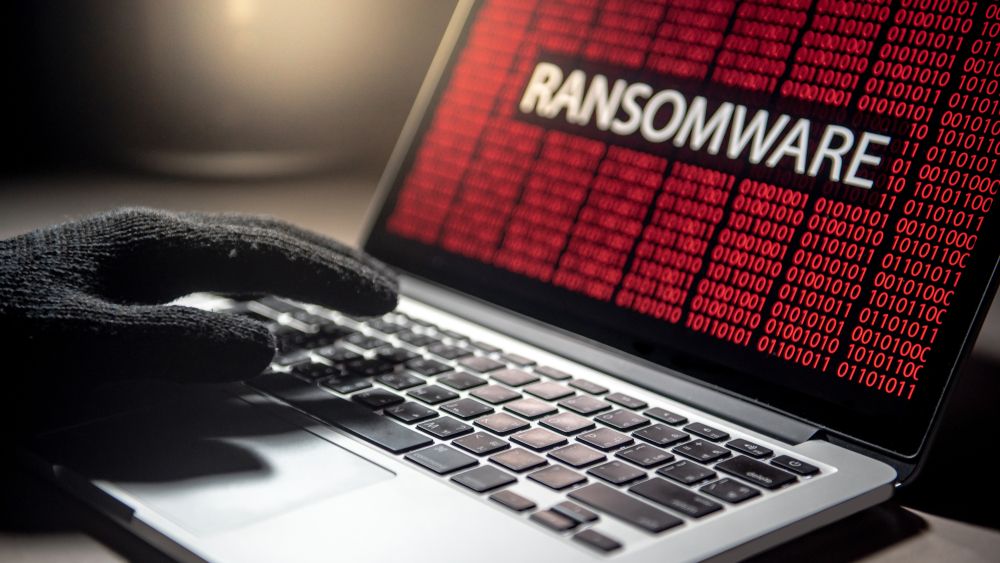 Male hacker hand on laptop computer keyboard with red binary screen of ransomware attack