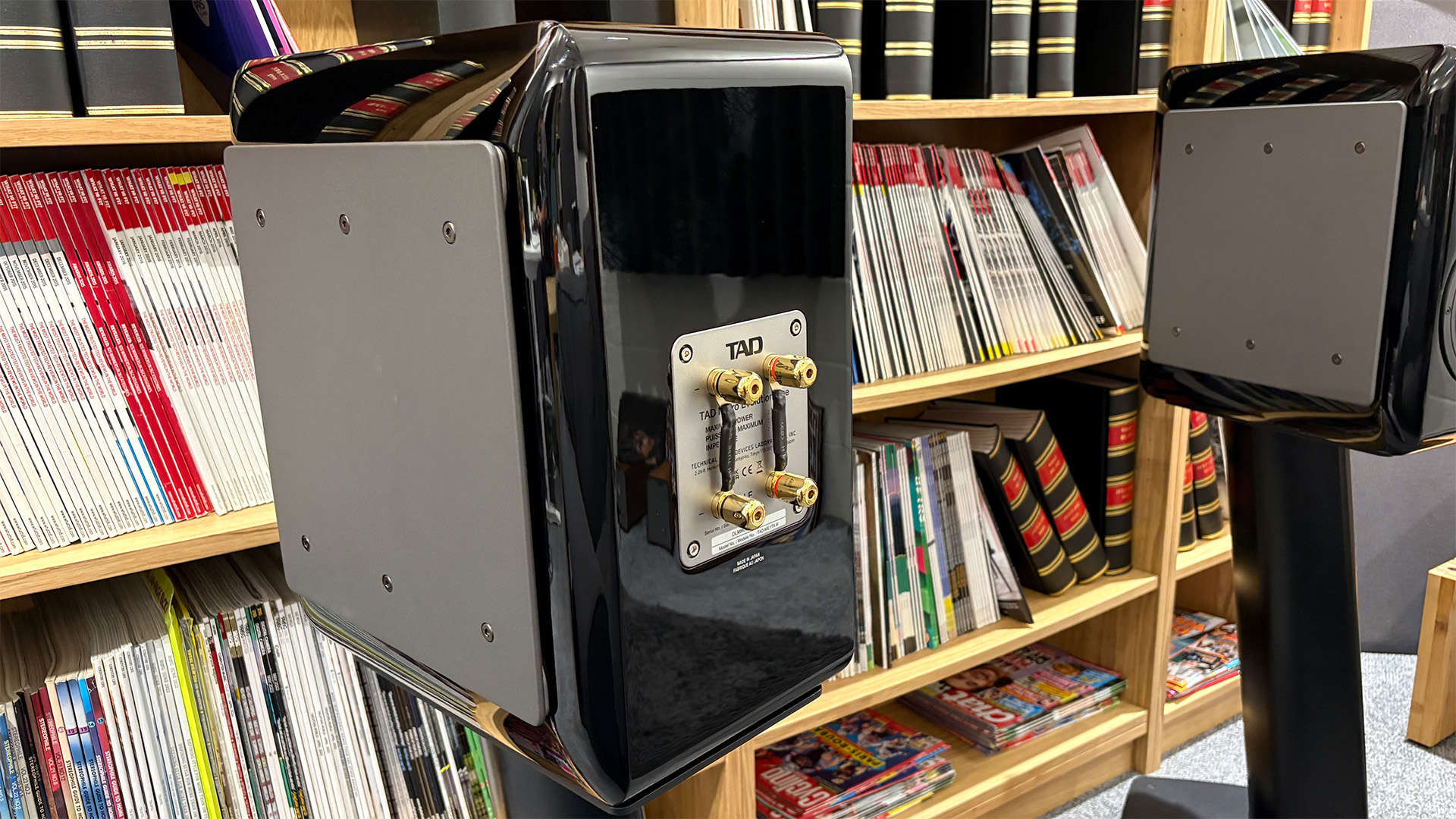 TAD ME1TX standmount speakers in front of bookcase, one speaker is turned around to show binding posts