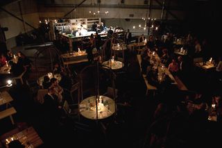 The interior of a restaurant with a dim light ambience and people sitting at their tables . photographed from above
