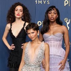 three woman in glamorous makeup and gowns in front of a blue and gold emmys step and repeat