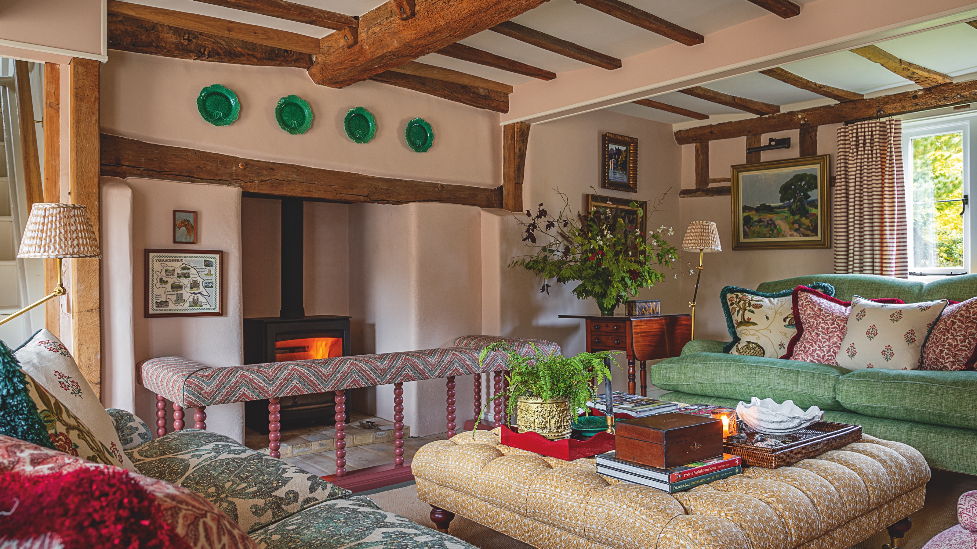 sitting room in English farmhouse with beamed ceiling, pink walls, large fireplace and upholstered furniture