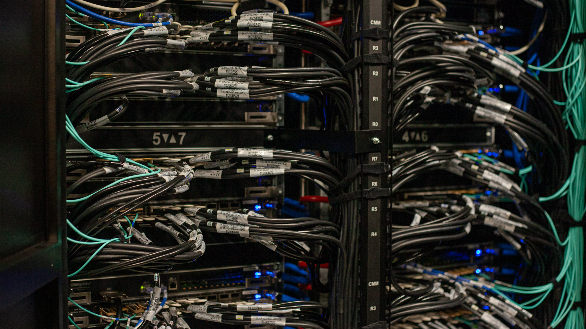 A shot of the HPE Slingshot 11 hardware used inside Isambard-AI, the UK&#039;s fastest supercomputer. Hundreds of cables link networking switches together inside a dark data center cabinet.