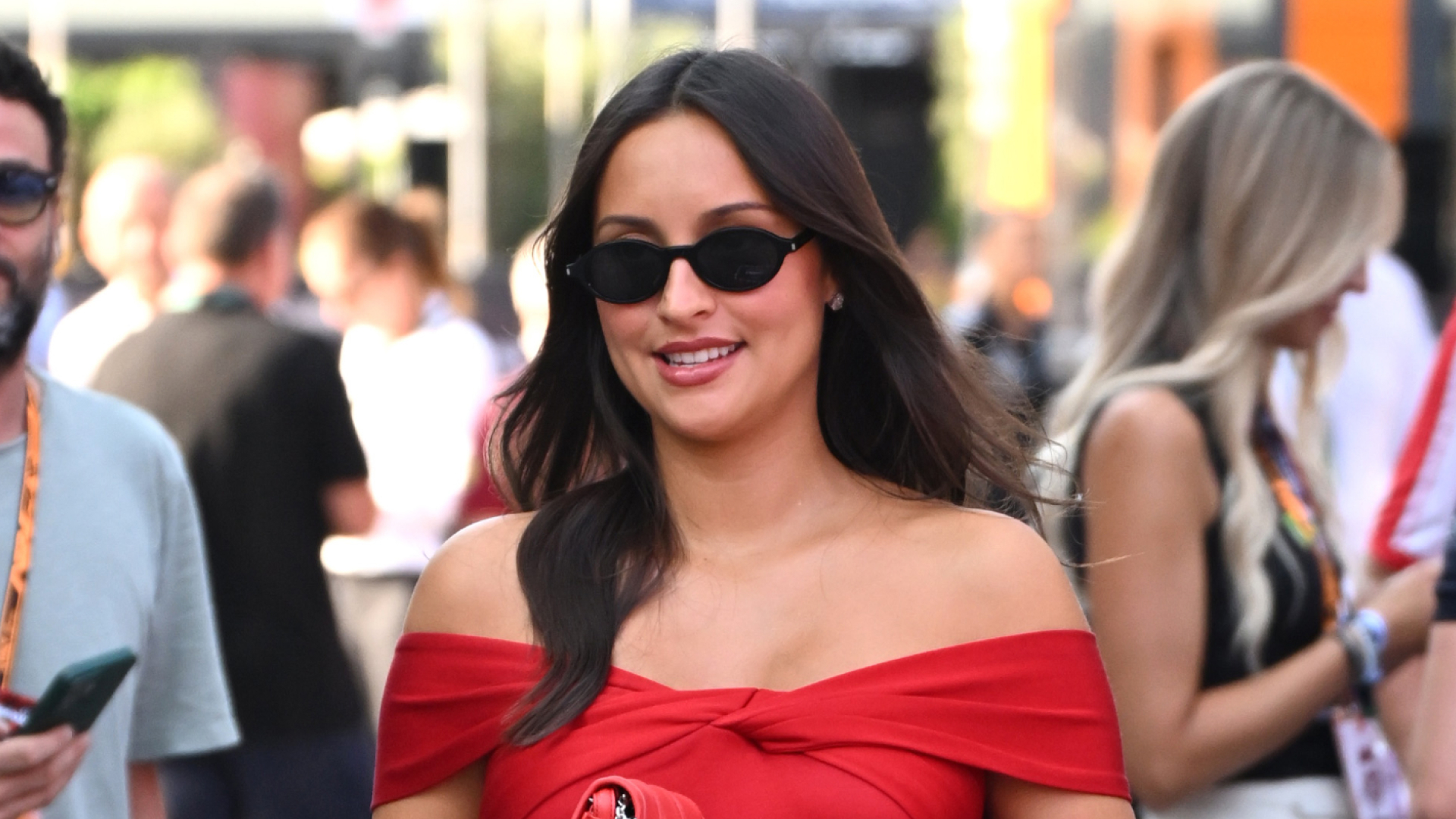 Alexandra Leclerc wearing a red Ferrari dress, she has long brown hair and is pregnant while wearing sunglasses
