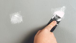 Hand holding filler knife and applying filler to grey wall