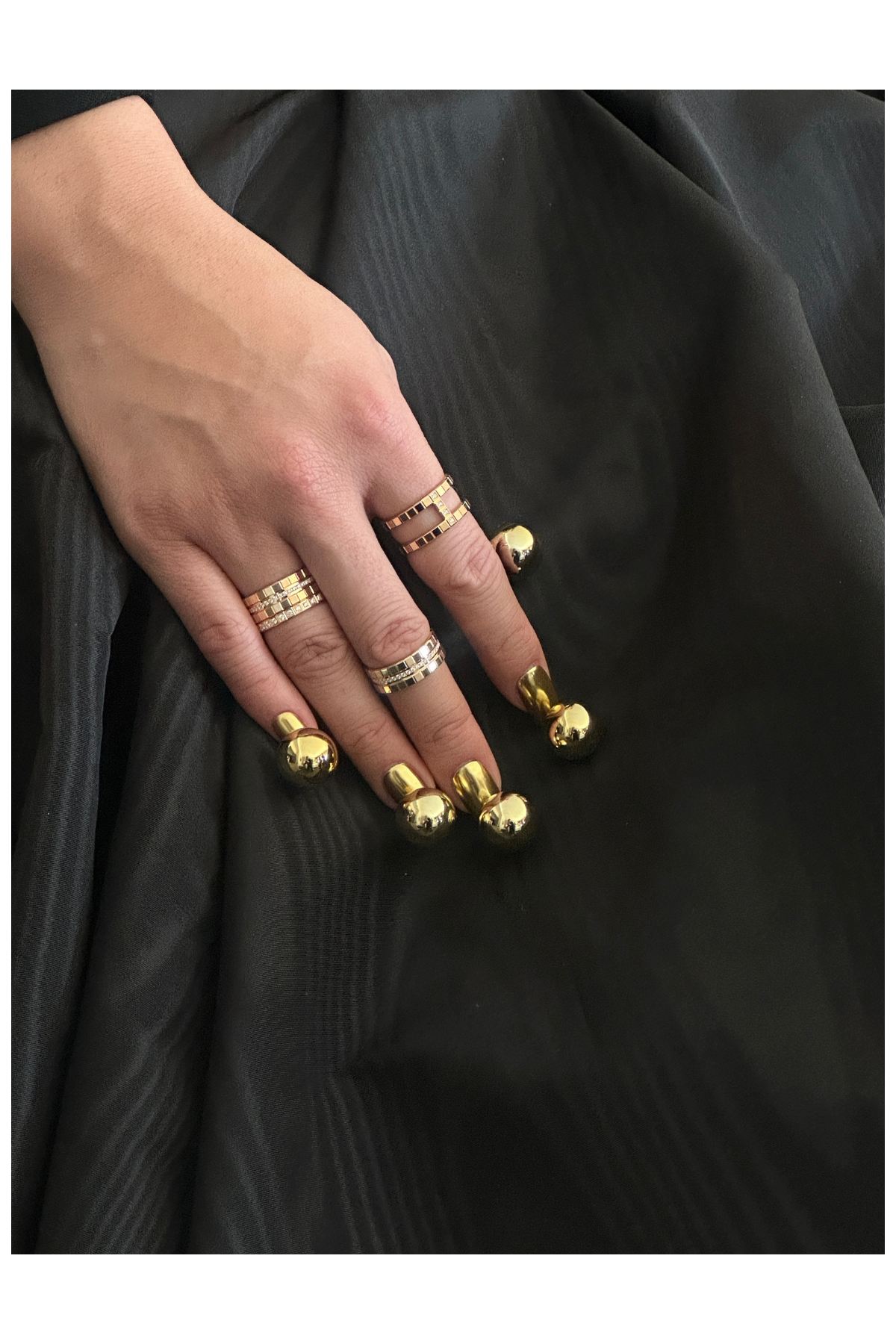 a manicure with gold orbs on a hand with rings against a black skirt