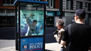 A person poses for a photograph with an artwork by street artist Banksy, the seventh to released this week, depicting fish swimming around a Police Box, in the City of London, on August 11, 2024