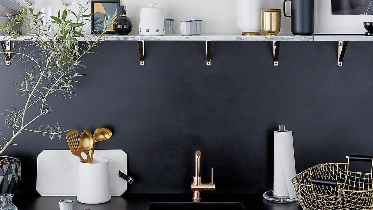 Matte White Utensil Holder from CB2 on black coutertop of dark blue kitchen beside sink with marble shelf above 