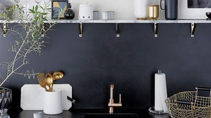 Matte White Utensil Holder from CB2 on black coutertop of dark blue kitchen beside sink with marble shelf above 