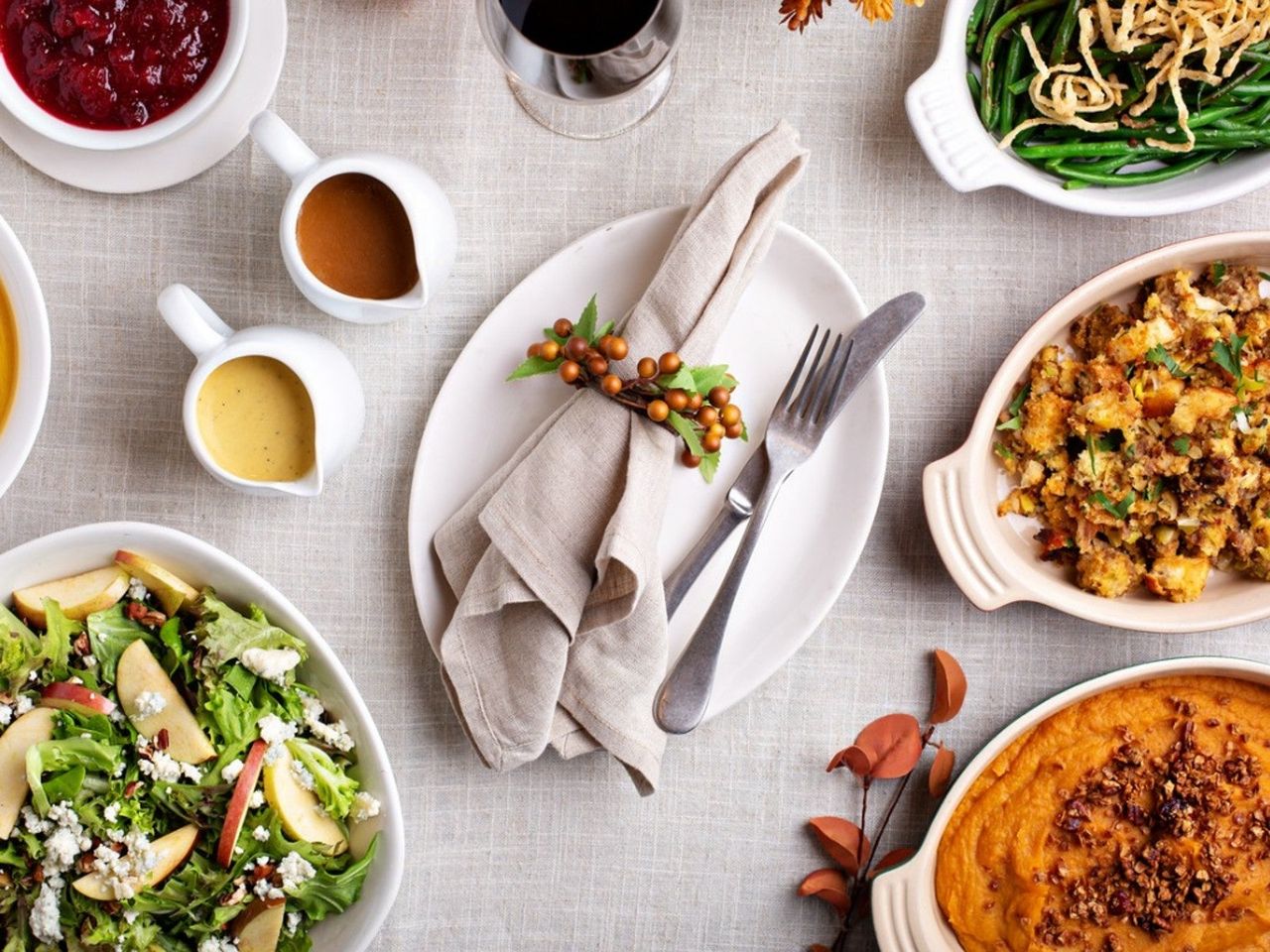 A napkin and silverware sit on a plate in the center of a table covered with autumnal, vegetarian dishes