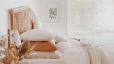 Outdated bedroom trends are so not it. Here is a white bedroom with a wooden bed, beige bedding, and a side table with flowers and books on top of it