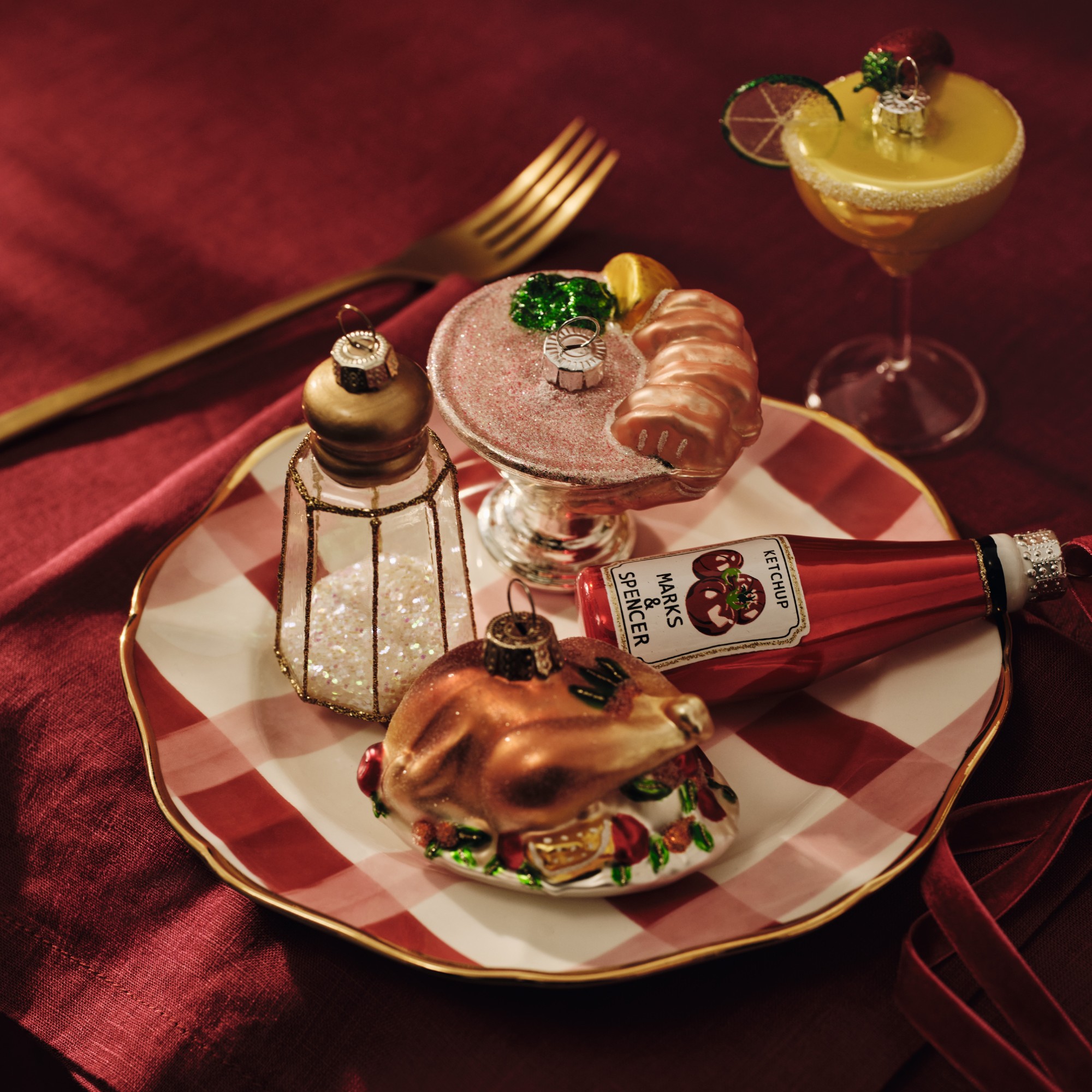 A checked dinner plate with food-shaped glass Christmas baubles on top
