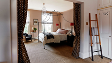 A peach bedroom with a black four-poster bed, polka dot curtains, and a blanket ladder against a linen closet