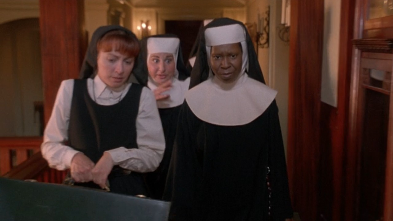 Whoopi Goldberg walking down the hall wearing a habit with two other nuns walking to her left.