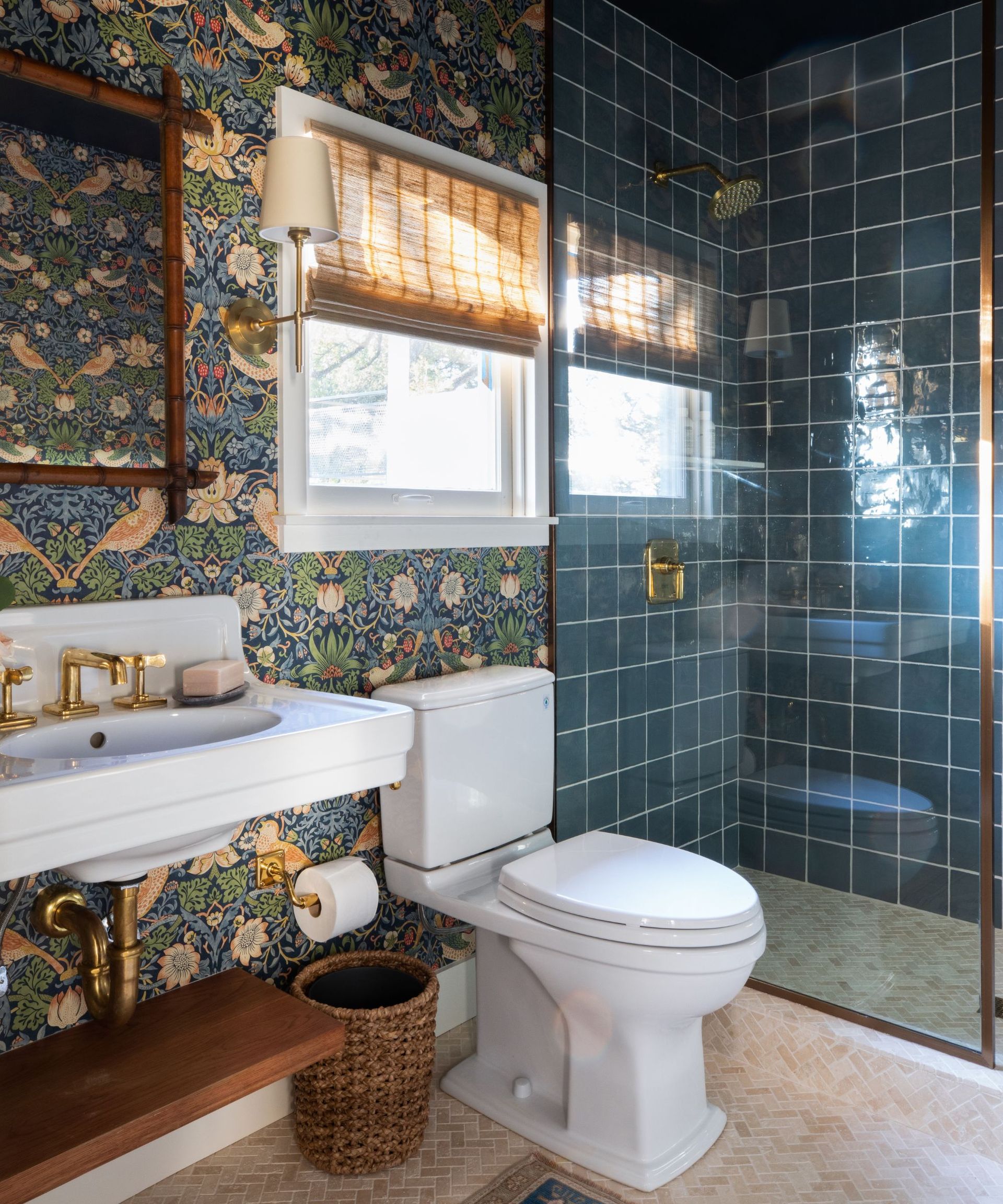 A small bathroom with a floating sink, strawberry thief wallpaper on the walls, and a walk-in shower with a glass screen and blue tiles