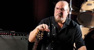 Steve Cropper photographed with his Peavey T-style, amp by his side, drums in the background.