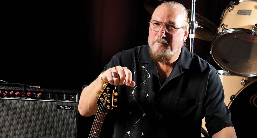 Steve Cropper photographed with his Peavey T-style, amp by his side, drums in the background.