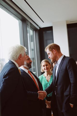 Prince Harry wearing a blue suit and shaking a man's hand