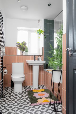 Small bathroom with pink vertical metro wall tiles, monochrome pattern floor tiles, white suite and green, pink and yellow floral bath mat