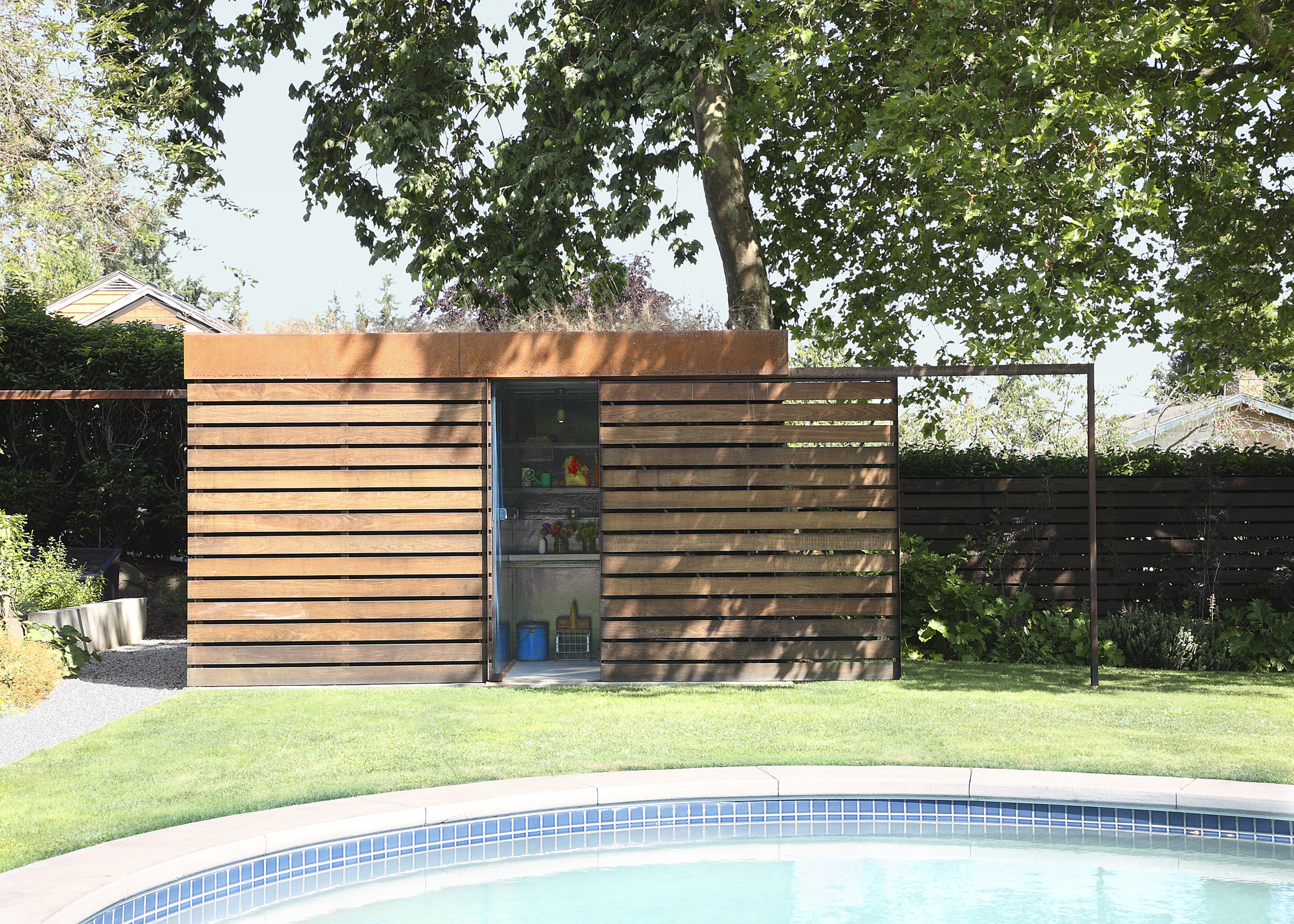 A garden shed with slatted panels (the same as the surrounding fence) and a sliding door to reveal the contents